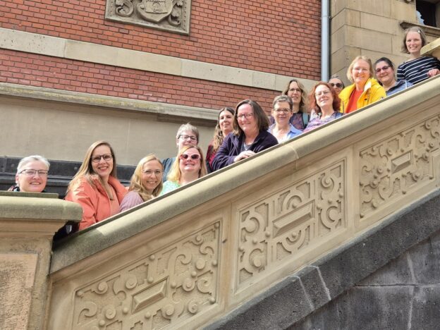 Die Mitglieder der RG Niedersachsen/Bremen stehen reihauf eine alte Treppe hinauf und schauen über das steinerne, verzierte Seitengeländer.