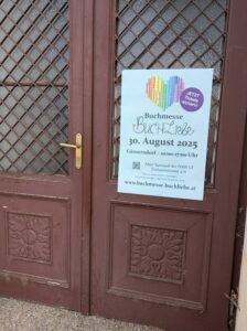 Braune Holztür mit Plakat der Buchmesse "Buchliebe" in Österreich: darauf ein Herz mit Regenbogenmuster
