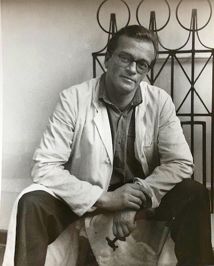 Schwarz-Weiß-Foto des noch jungen Künstlers Bodo Kampmann, der mit weißem Kittel auf einem Hocker sitzt