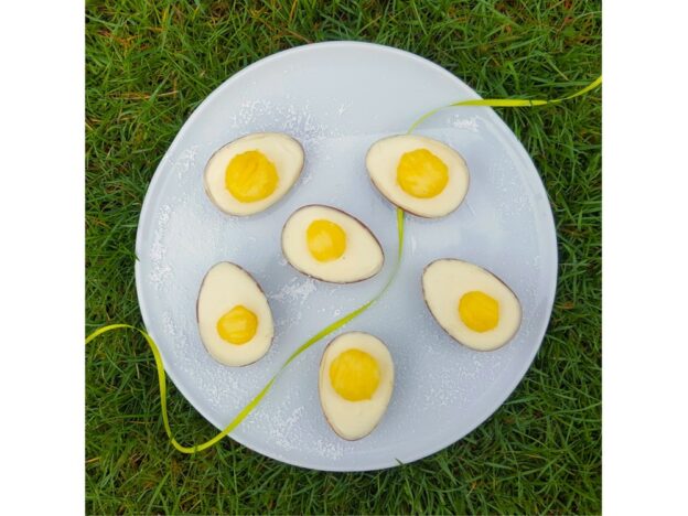 Mit weißer Schokolade und Eidotter aus Obst gefüllte Überraschungseier liegen auf einem Teller, der auf grünem Grad liegt