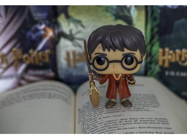 Eine Harry-Potter-Figur mit übergroßem Kopf steht auf einem aufgeschlagenen Buch. Dahinter sind mehrere Harry-Potter-Bücher aufgestellt