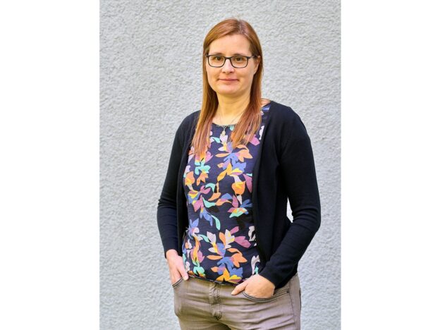 Inga Beißwänger, langjährige Pressesprecherin des VFLL mit buntem T-Shirt und dunkler Strickjacke vor grauem Hintergrund