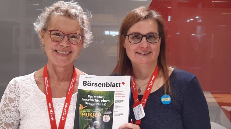 Foto von Sibylle Schütz und Inga Beißwänger mit VFLL-Umhängern und der Ausgabe des Magazine "Börsenblatt" in der Hand. Beide lächeln in die Kamera